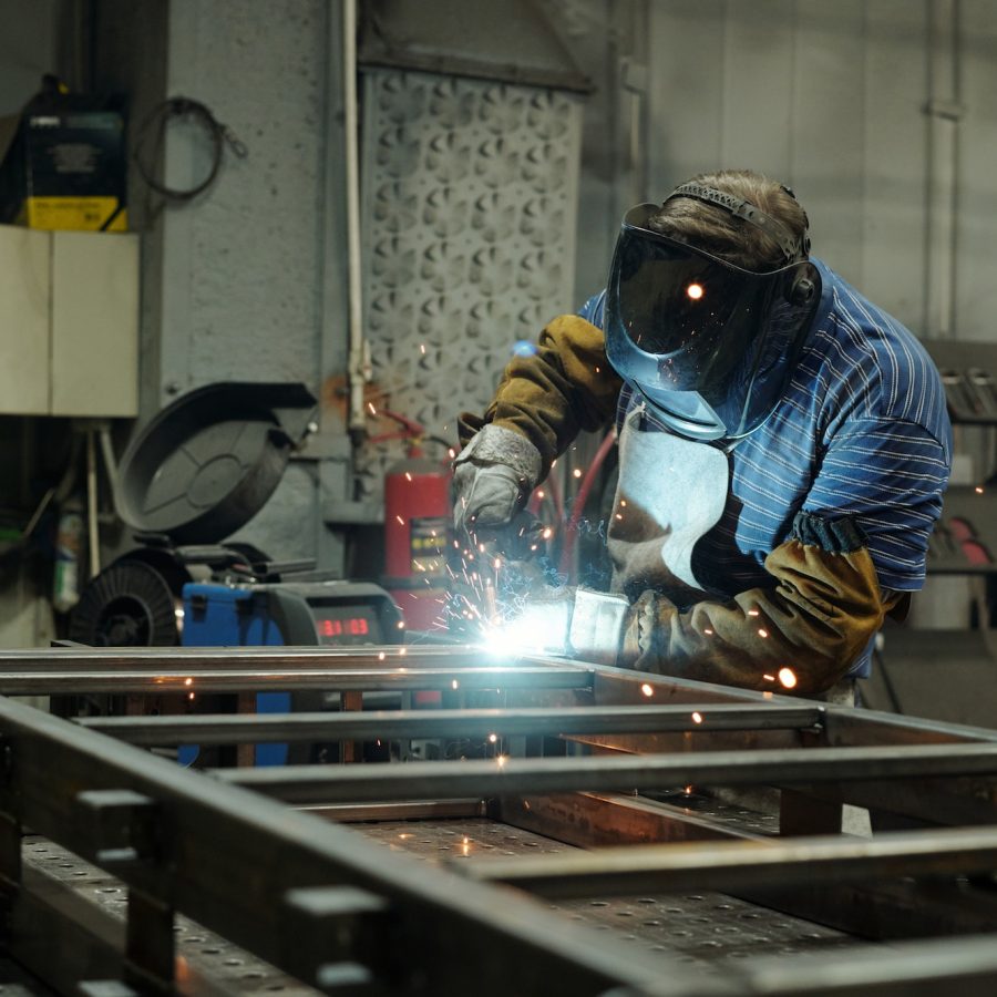 Young male welder in protective mask and gloves welding metallic structure